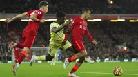 Pemain Arsenal Bukayo Saka (tengah) berebut bola dengan pemain Liverpool Kostas Tsimikas (kiri) dan Thiago pada pertandingan sepak bola Liga Inggris di Stadion Anfield, Liverpool, Inggris, 20 November 2021. Liverpool menang 4-0. (AP Photo/Jon Super)