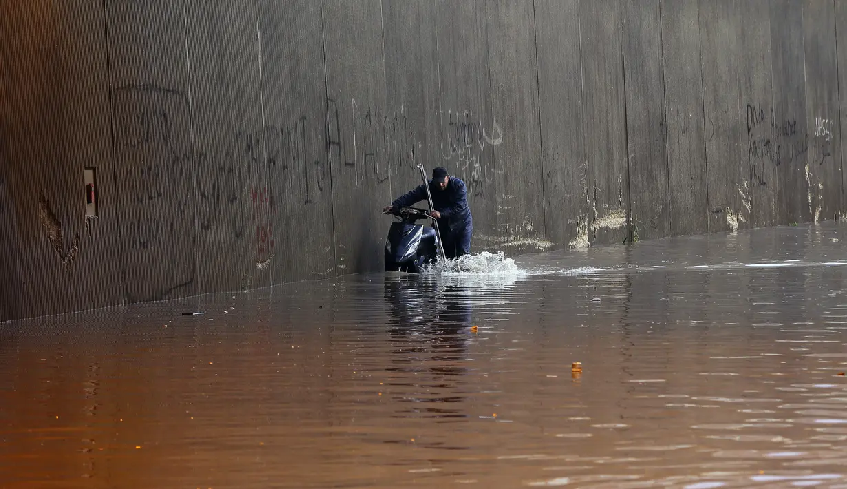 Seorang pria mendorong sebuah skuter yang mogok di dalam terowongan banjir di pinggiran selatan Beirut Ouzai, Lebanon (9/12/2019). Hujan deras membuat sejumlah rumah dan kendaraan di Lebanon terendam banjir dan melumpuhkan daerah-daerah dari ibukota Beirut, Lebanon. (AP Photo/Bilal Hussein)