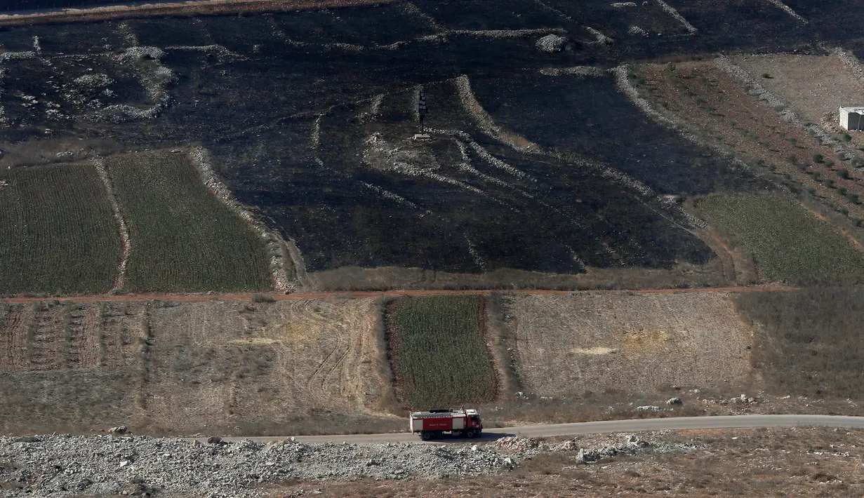 Sebuah truk pemadam kebakaran Lebanon melewati perbatasan dengan Israel di sebelah ladang yang terbakar usai serangan artileri berat Israel di desa perbatasan Maroun Al-Ras, Lebanon, Senin (2/9/2019). (AP Photo/Hussein Malla)