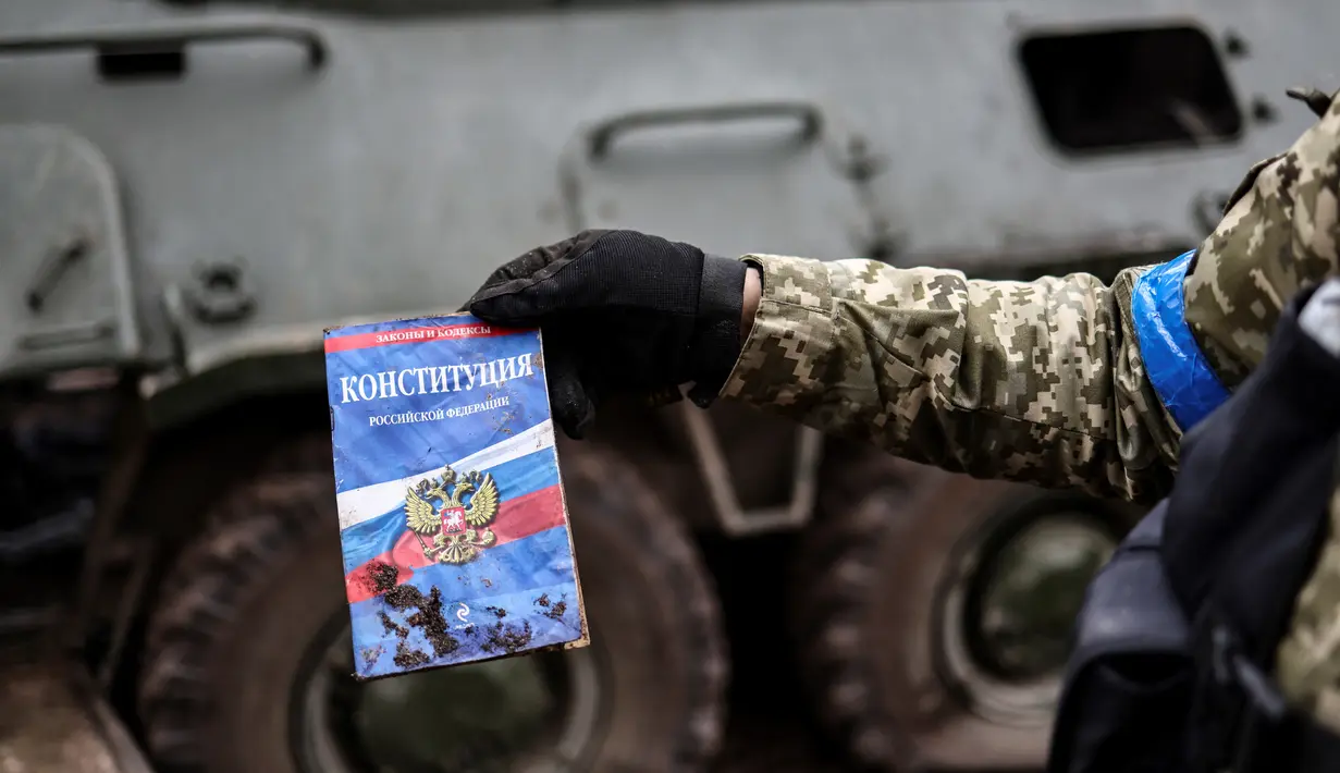 Seorang anggota tentara Ukrania menunjukkan sebuah konstitusi Rusia yang ditemukan di kamp pangkalan Rusia yang kosong di dekat Buda-Babynetska, utara Kiev,pada 5 April 2022, beberapa hari setelah pasukan Rusia mundur. (RONALDO SCHEMIDT / AFP)