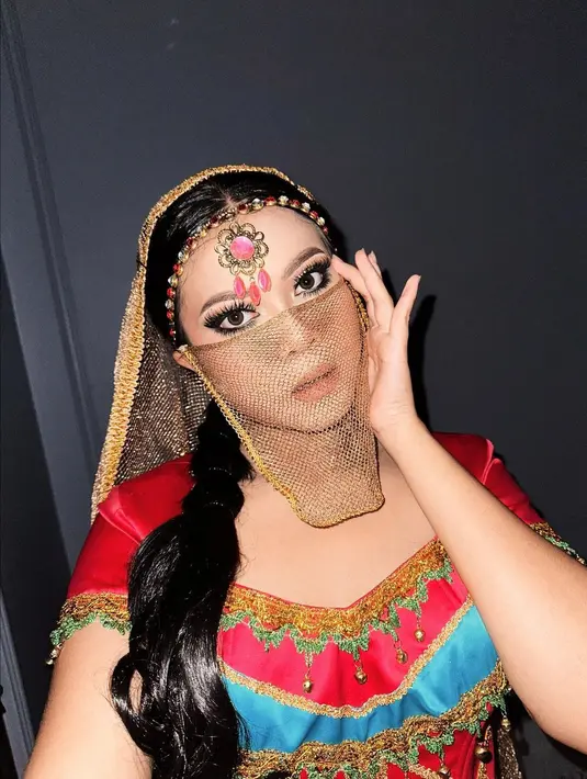 Lagi, tampil bak Arabian Princess, kali ini Hanum Mega mengenakan outfit berbeda. Bak Princess Jasmin dalam outfit merah, Hanum menghadirkan makeup look dengan mempertajam area mata dan nuansa nude pada bibir dan pipi. Ia juga mengenakan wig yang kemudian ditutup kerudung emas, headpiece bak pengantin India, lengkap dengan penutup wajah semi transparan. Foto: Instagram.