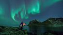 Seorang peselancar menatap Aurora sebelum beraksi di Lofoten Islands, Norwegia, (9/3/2018). Suhu udara minus 13°C dan suhu diatas air sekitar 4°C. (AFP/Oliver Morin)