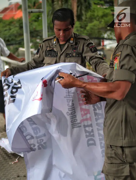 Petugas Satpol PP menertibkan alat peraga kampanye (APK) di jembatan penyeberangan orang (JPO) kawasan Gambir, Jakarta, Sabtu  (22/12). Penertiban itu dilakukan karena melanggar aturan pemasangan dari komisi pemilihan umum. (Liputan6.com/Faizal Fanani)
