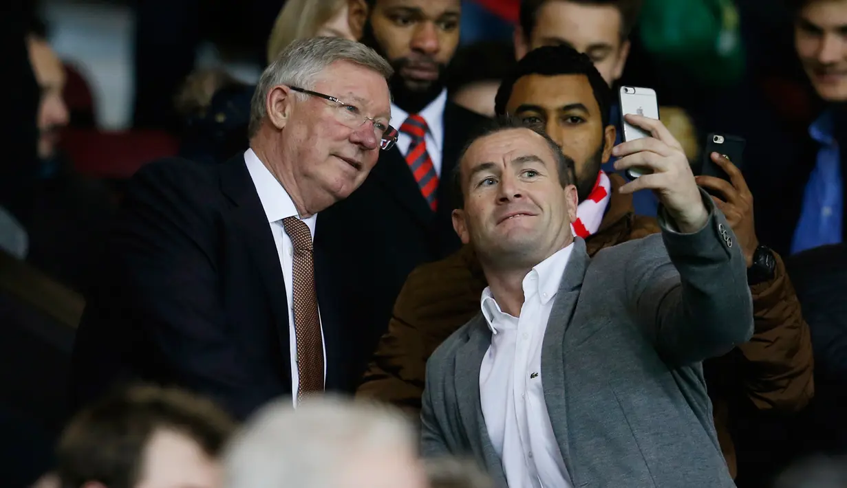 Mantan manajer Manchester United Sir Alex Ferguson berselfie dengan fans saat menyaksikan pertandingan antara Manchester United dengan Chelsea di Stadion Old Trafford, Inggris (28/12). MU bermain imbang dengan Chelsea dengan skor 0-0. (Reuters/Phil Noble)