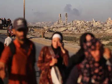 Asap membubung di atas bangunan-bangunan yang hancur saat warga Palestina meninggalkan kota Gaza ke arah selatan dengan membawa barang-barang mereka, melalui jalan pesisir dekat kamp pengungsi Nuseirat di bagian tengah Jalur Gaza, pada 12 September 2025. (Eyad BABA/AFP)