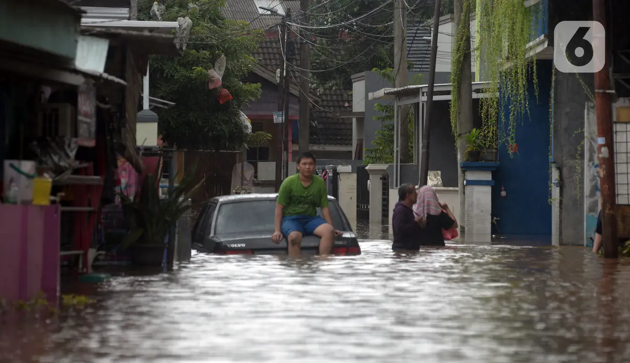 Warga duduk di atas mobil saat banjir merendam jalan dan rumah di RT 003/05, Pejaten, Jakarta, Sabtu ( 20/2/2021). Curah hujan yang tinggi sejak malam hingga dini hari mengakibatkan sejumlah kawasan terendam banjir. (merdeka.com/Imam Buhori)
