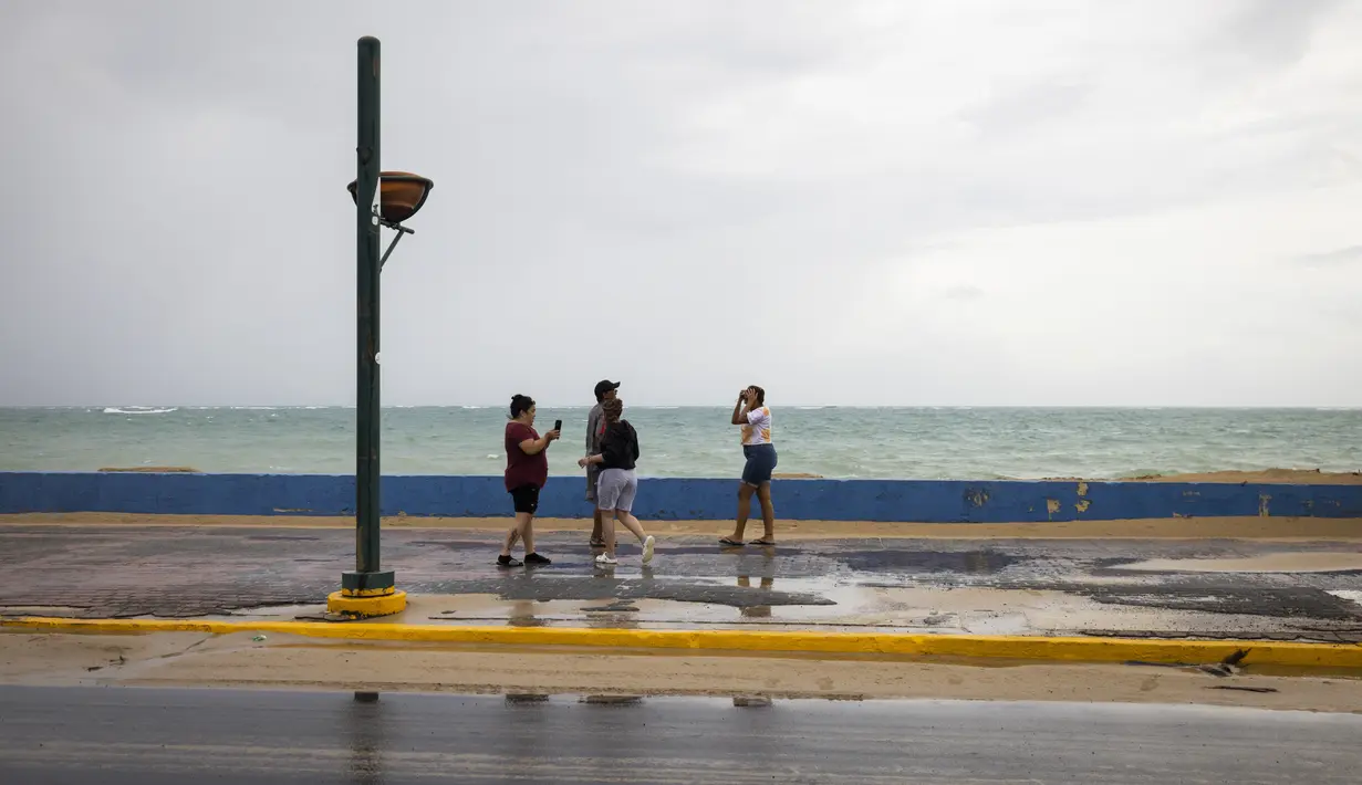 Sekelompok wisatawan berjalan di dekat laut sebelum kedatangan Badai Tropis Fiona di San Juan, Puerto Rico, Sabtu (17/9/2022). Setelah dari Puerto Rico, Fiona diproyeksikan melintasi Republik Dominika pada Senin mendatang dengan ancaman hujan deras yang berpotensi memicu banjir bandang atau longsor. (AP Photo/Alejandro Granadillo)