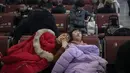 Seorang wanita dan anak kecil tertidur saat menunggu jadwal keberangkatan kereta di stasiun Beijing, Selasa (29/1). Jutaan orang meninggalkan kota-kota besar China menuju kampung halaman, guna merayakan Imlek pada Februari mendatang. (Nicolas ASFOURI/AFP)