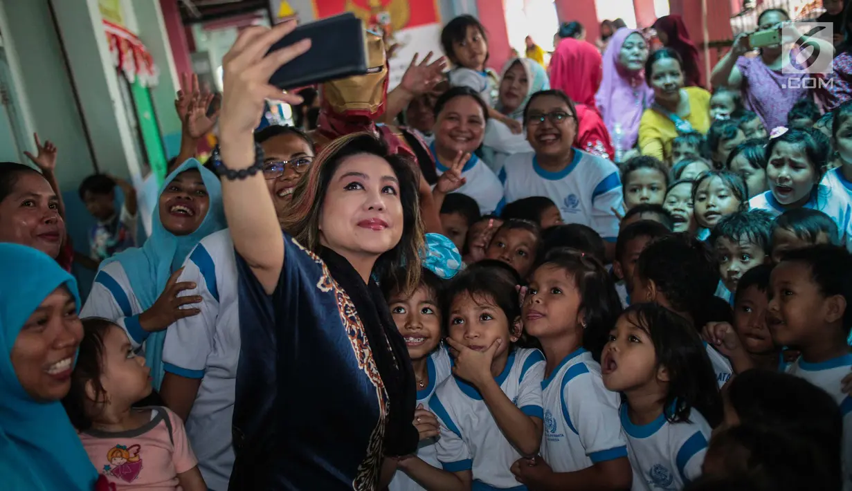 Pendiri Yayasan Pansophia Nusantara, Millie Lukito berselfie dengan anak-anak Pendidikan anak usia dini (PAUD) Cahaya Permata Indonesia (CPI) di Rusunawa Marunda, Jakarta Utara, Jumat (30/11). (Liputan6.com/Faizal Fanani)