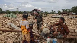 Di desa Lintang Baru, Aceh Tamiang, ada banyak rumah dan bangunan hilang tertimbun kayu gelondongan dan material lumpur yang mulai mengeras. Tampak dalam foto, warga beristirahat sambil mencari sisa-sisa rumah mereka yang terkubur di bawah tumpukan pohon tumbang yang disapu banjir bandang, di desa Lintang Baru di Aceh Tamiang, Sumatera Utara, pada Kamis 11 Desember 2025. (Aditya Aji/AFP)