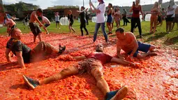 Peserta berbaring di atas tomat yang hancur ketika berpartisipasi dalam festival 'Tomatina' di St.Petersburg, Rusia, Minggu (18/8/2019). Tomatina atau perang tomat adalah festival Spanyol, dan tahun ini merupakan pertama kalinya dirayakan di Rusia. (AP Photo/Dmitri Lovetsky)