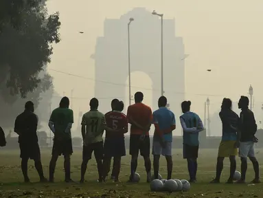 Sejumlah pria mendengarkan pelatih sebelum bermain sepak bola di tengah kondisi kabut asap tebal di New Delhi, India (30/10). Tingkat kabut melonjak selama musim dingin di Delhi, ketika kualitas udara memburuk. (AFP Photo/Prakash Singh)