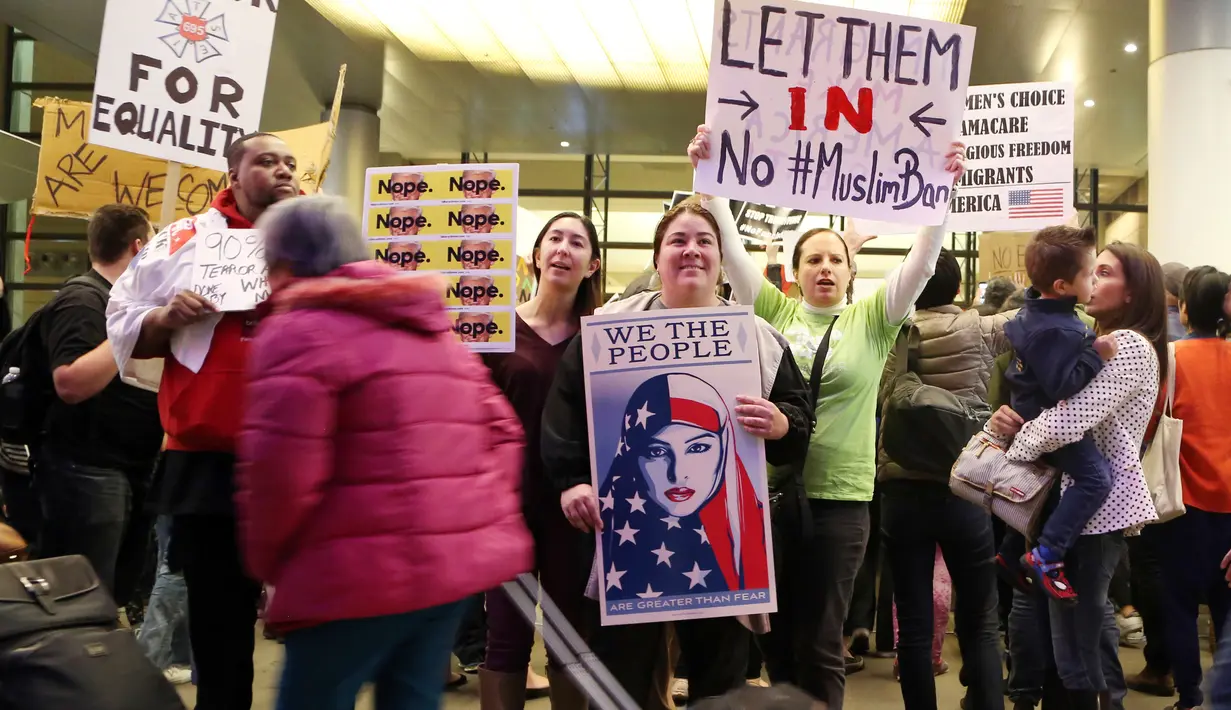 Calon penumpang melewati massa yang menggelar aksi protes di Terminal Internasional Tom Bradley, Bandara LAX, Los Angeles, Sabtu (28/1). Mereka menggelar aksi protes terkait kebijakan Presiden AS Donald Trump tentang imigrasi. (AP Photo/Reed Saxon)