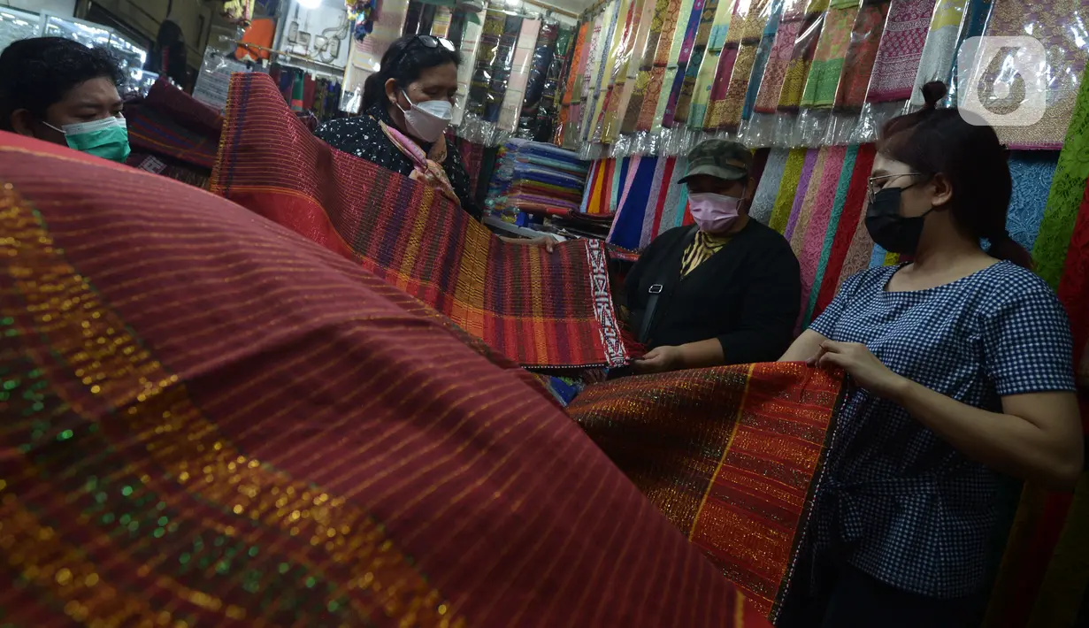 Pembeli melihat-lihat kain ulos di pasar proyek Senen, Jakarta, Kamis (21/10/2021). Sejak status PPKM turun menjadi level 2, pengunjung ramai mendatangi toko membeli kain ulos untuk upacara pernikahan adat dengan kisaran harga dari Rp. 500.000 hingga jutaan rupiah. (merdeka.com/Imam Buhori)