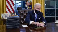 Presiden Joe Biden meraih pena untuk menandatangani perintah eksekutif pertamanya di Ruang Oval, Gedung Putih di Washington, Rabu (20/1/2021). Pada hari pertamanya menjabat, Presiden Amerika Serikat Joe Biden menandatangani sejumlah tindakan eksekutif di Gedung Putih. (AP Photo/Evan Vucci)