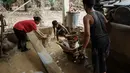 Pembersihan rumah dan barang-barang dilakukan agar mereka dapat segera kembali ke rumah setelah mengungsi. Tampak dalam foto, Panji (kanan), 23 tahun, membawa lumpur keluar dari dapur menggunakan gerobak dorong di rumah orang tuanya, setelah banjir bandang, di Aceh Tamiang, Minggu 14 Desember 2025. (Yasuyoshi CHIBA/AFP)