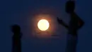 Warga berdiri dengan latar belakang supermoon yang terlihat di Pantai Sanur, Bali, Senin (14/11). Fenomena ini terjadi saat bulan mencapai titik terdekat dengan bumi dan merupakan fenomena supermoon terbesar dalam 68 tahun terakhir. (SONNY TUMBELAKA/AFP)
