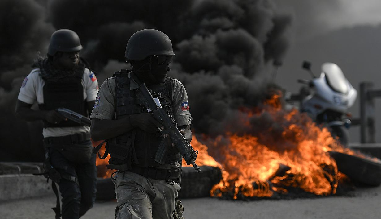 Polisi bersenjata berlindung dekat barikade yang dibakar saat demonstrasi menuntut keadilan atas pembunuhan Presiden Haiti Jovenel Moise di Cap-Haitien, Haiti, Kamis (22/7/2021). Demonstrasi menuntut keadilan atas pembunuhan Jovenel Moise terus berlanjut. (AP Photo/Matias Delacroix)