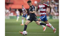 Pemain Real Madrid, Arda Guler (kiri) menggiring bola dibayangi pemain Granda, Kamil Piatkowski pada laga lanjutan Liga Spanyol 2023/2024 di Nuevo Los Carmenes Stadium, Granada, Sabtu (11/05/2024). (AFP/Jorge Guerrero)