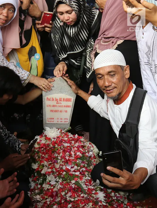 Seorang pria berswafoto dengan latar belakang batu nisan Presiden ketiga BJ Habibie di Taman Makam Pahlawan Nasional Kalibata, Jakarta, Kamis (12/9/2019). Selain berdoa, tidak sedikit juga warga  mengabadikan dengan kamera ponsel. (Liputan6.com/Herman Zakharia)