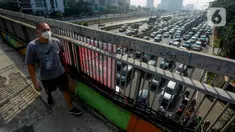 Pejalan kaki yang mengenakan masker berjalan di atas jembatan penyeberangan orang (JPO) dengan arus lalu lintas yang macet di kawasan Jalan TB Simatupang, Jakarta, Rabu (15/8/2023). Kementerian Lingkungan Hidup dan Kehutanan (KLHK) menilai, sumber pencemaran kualitas udara alias polusi udara Jakarta dan sekitarnya masih didominasi oleh sektor transportasi. (merdeka.com/Arie Basuki)