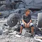 Seorang anak laki-laki Palestina duduk di reruntuhan bangunannya yang hancur akibat serangan udara Israel di Kamp Nuseirat, Jalur Gaza, Palestina, 16 Oktober 2023. (AP Photo/Hatem Moussa)