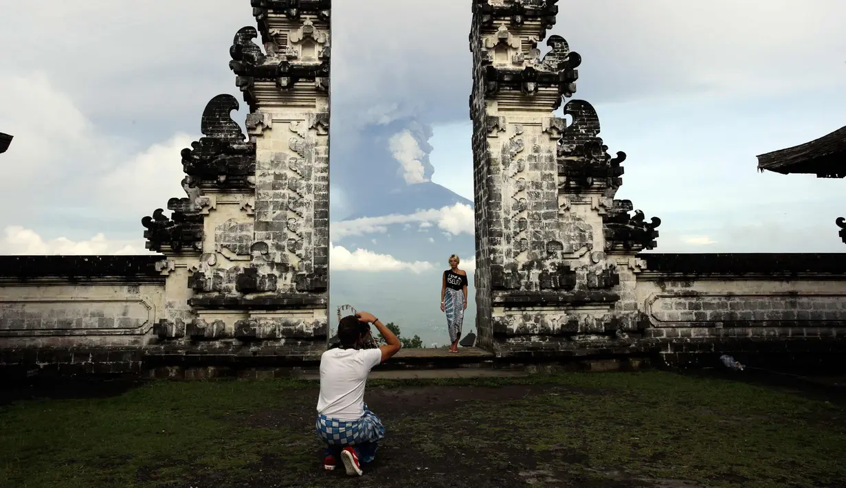 <p>Turis asing foto di depan Gunung Agung yang meletus di Kabupaten Karangasem, Bali, (27/11). Sebelumnya, Gunung Agung telah mengalami erupsi sejak Sabtu (25/11) sore. (AP Photo / Firdia Lisnawati)</p>