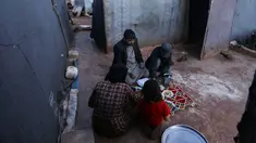 Pengungsi Suriah berkumpul di depan tenda untuk berbuka puasa dengan makanan yang didistribusikan organisasi amal lokal selama bulan suci Ramadhan, di kamp pengungsi di pinggiran kota Dana yang dikuasai pemberontak, timur perbatasan Turki-Suriah di Idlib (3/4/2022). (AFP/Aaref Watad)