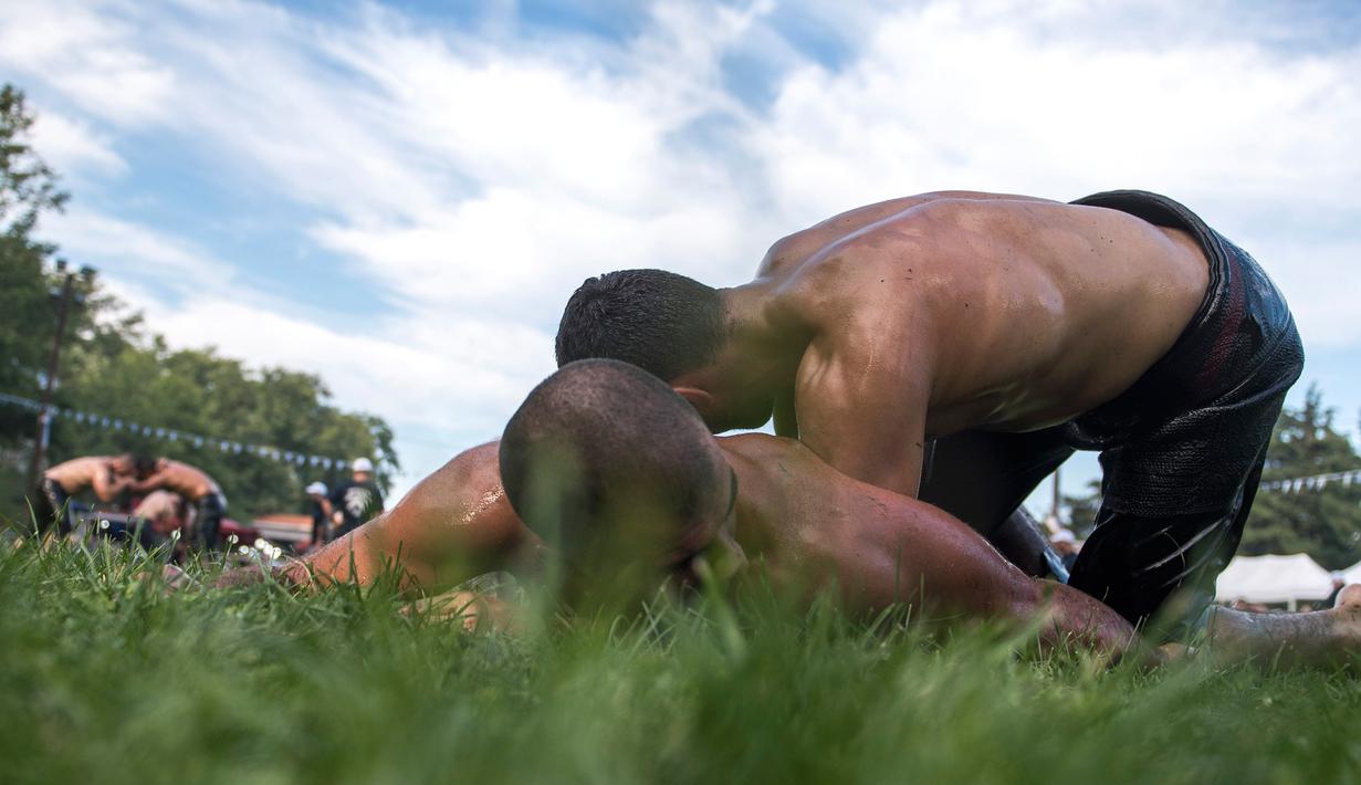 Pegulat saling kunci dengan lawannya dalam kompetisi tahunan gulat minyak tradisional di Sochos, Yunani, 30 Juni 2018. Lebih dari seratus drum minyak zaitun habis untuk melumuri sekujur tubuh setiap peserta. (AP/Giannis Papanikos)