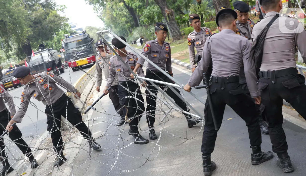 Personel Kepolisian merapatkan barikade kawat berduri yang menutup ruas Jalan Medan Merdeka Barat, Jakarta, Senin (28/10/2019). Penutupan ini antisipasi aksi unjuk rasa mahasiswa mendesak Presiden Jokowi segera mengeluarkan Perppu KPK. (Liputan6.com/Helmi Fithriansyah)