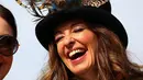 Seorang wanita tertawa saat tiba pada hari pertama Festival Cheltenham di Cheltenham Racecourse, di Cheltenham, Inggris (15/3/2022). Kehadiran para wanita memberikan nuansa tersendiri di kompetisi pacuan kuda tersebut. (AFP/Adrian Dennis)