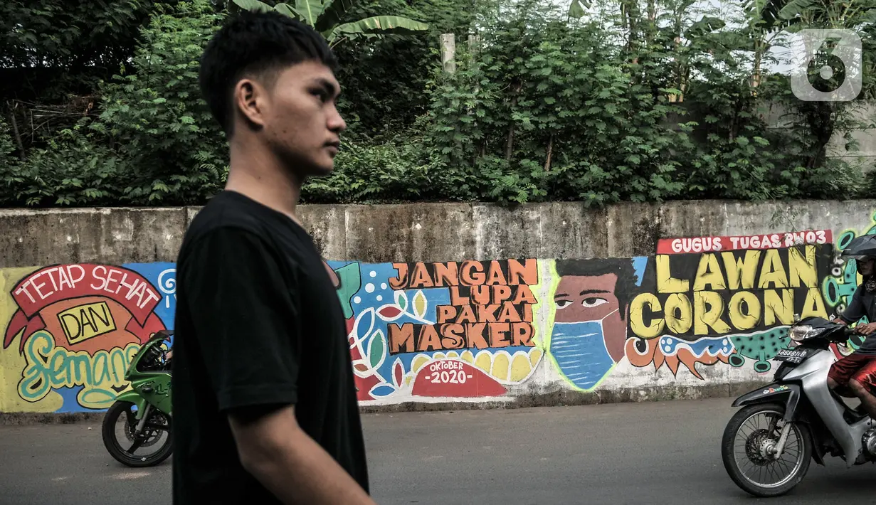Warga melintasi mural bertema imbauan protokol kesehatan COVID-19 di kawasan Cakung Barat, Jakarta, Minggu (18/10/2020). Mural karya warga setempat tersebut bertujuan mengingatkan masyarakat akan pentingnya memakai masker, menjaga jarak, dan mencuci tangan. (merdeka.com/Iqbal S. Nugroho)