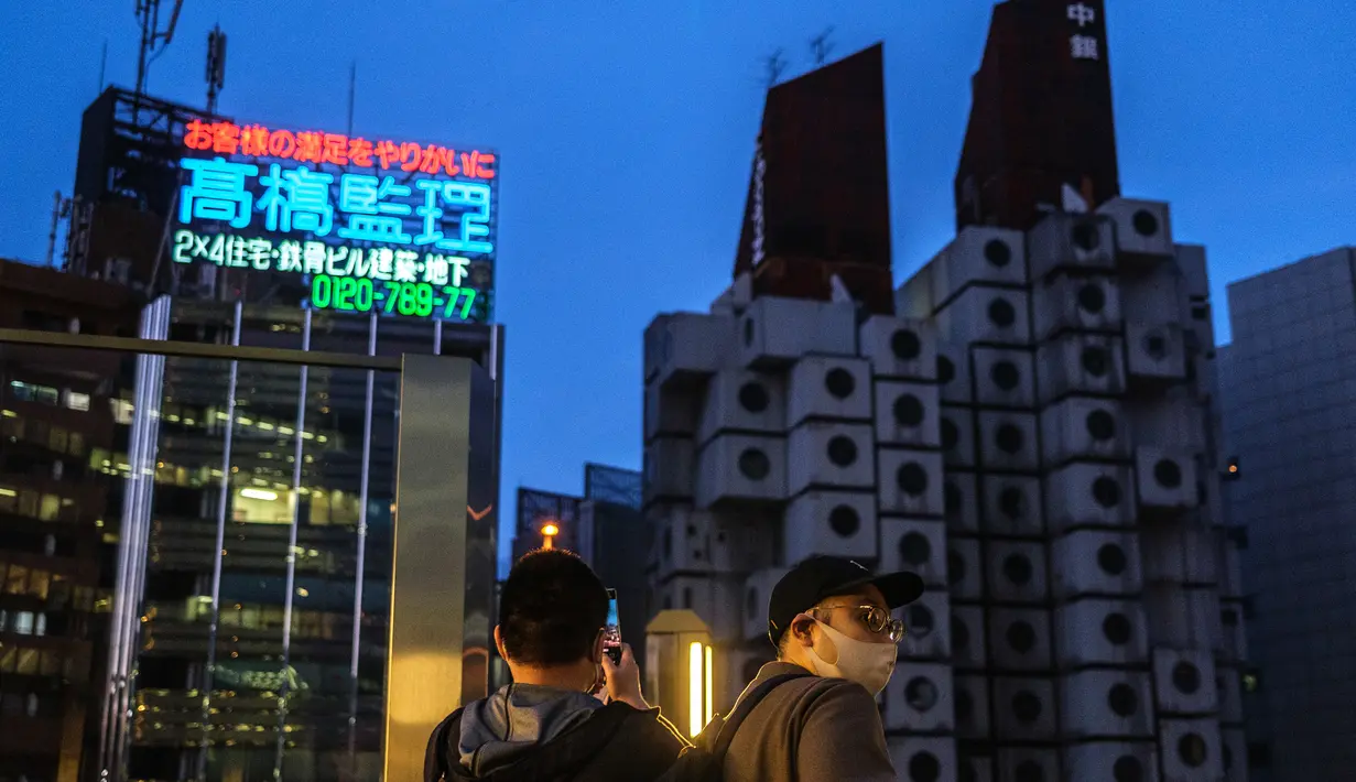 Orang-orang memotret Nakagin Capsule Tower (kanan), sebuah bangunan perumahan dan perkantoran serba guna di distrik Ginza Tokyo, 6 April 2022. Menara yang selesai pada tahun 1972 dan dirancang oleh arsitek terkenal Kisho Kurokawa itu adalah sebuah landmark dari gerakan Metabolisme. (Philip FONG/AFP)