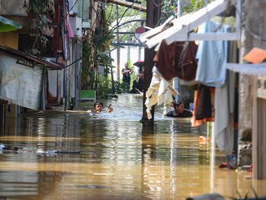 Warga beraktifitas saat banjir merendam pemukiman di Jalan Pirus, Kelurahan Bidara Cina, Jatinegara, Jakarta Timur, Minggu (6/7/2025). (merdeka.com/Arie Basuki)