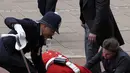 Dengan suhu mencapai 24C, menurut Met Office, seorang prajurit muda harus dibantu berdiri oleh petugas polisi setelah pingsan sebelum upacara dimulai. (Kirsty Wigglesworth / POOL / AFP)