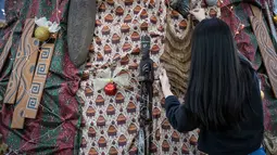Instalasi dekorasi Pohon Natal ini berdiri setinggi tujuh meter dengan diameter 3,3 meter dan dibuat dari rangka kayu serta kain bermotif khas Papua. Tampak dalam foto, salah satu mahasiswa memasang sentuhan akhir pada instalasi dekorasi berbentuk pohon Natal dengan motif budaya Papua di Perpustakaan Petra Christian University (PCU), Surabaya, Jawa Timur, Kamis 18 Desember 2025. (JUNI KRISWANTO/AFP)