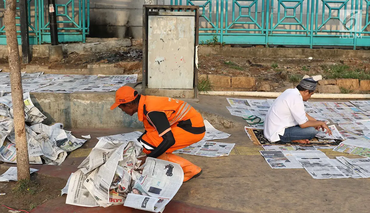 Petugas kebersihan memungut koran usai salat id Hari Raya Idul Fitri 1 Syawal 1439 H di kawasan Senen, Jakarta, Jumat (15/6). Banyaknya koran berserakan membuat petugas harus sigap membersihkan agar tidak mengotori jalan. (Liputan6.com/Immanuel Antonius)