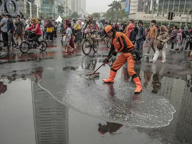 Petugas Penanganan Prasaran dan Sarana Umum (PPSU) membersihkan genangan air saat car free day (CFD) di kawasan Bundaran HI, Jakarta, Minggu (29/12/2019). Pembersihan genangan air dilakukan agar warga yang sedang berolahraga di kawasan tersebut nyaman. (Liputan6.com/Faizal Fanani)