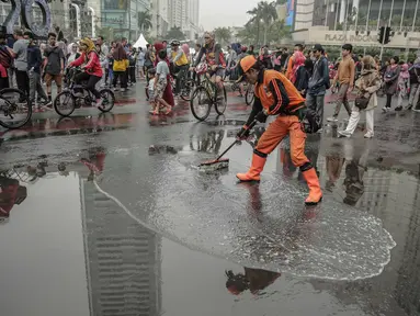Petugas Penanganan Prasaran dan Sarana Umum (PPSU) membersihkan genangan air saat car free day (CFD) di kawasan Bundaran HI, Jakarta, Minggu (29/12/2019). Pembersihan genangan air dilakukan agar warga yang sedang berolahraga di kawasan tersebut nyaman. (Liputan6.com/Faizal Fanani)
