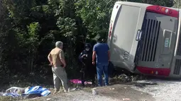 Petugas kepolisian dan paramedis memeriksa lokasi kecelakaan sebuah bus wisata yang terbalik di Quintana Roo, Meksiko, Selasa (19/12). Sebanyak 7 korban luka merupakan warga negara AS dan dua lainnya berkebangsaan Swedia. (Manuel Jesús ORTEGA CANCHE/AFP)