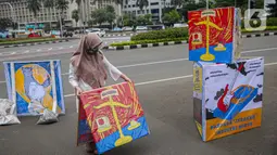 Seorang yang tergabung dalam Koalisi Masyarakat Peduli Kesehatan (KOMPAK) menunjukkan poster saat menggelar aksi #ParadeMural di kawasan Patung Arjuna Wijaya, Jakarta, Rabu (17/11/2021). Aksi juga dilakukan untuk menyambut Hari Kesehatan Nasional 2021. (Liputan6.com/Faizal Fanani)