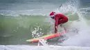Seorang pengunjung berkostum Sinterklas berselancar dalam acara Surfing Santa yang berlangsung di Pantai Cocoa, Florida, Amerika Serikat, Selasa (24/12/2024) waktu setempat. (AFP/Giorgio Viera)
