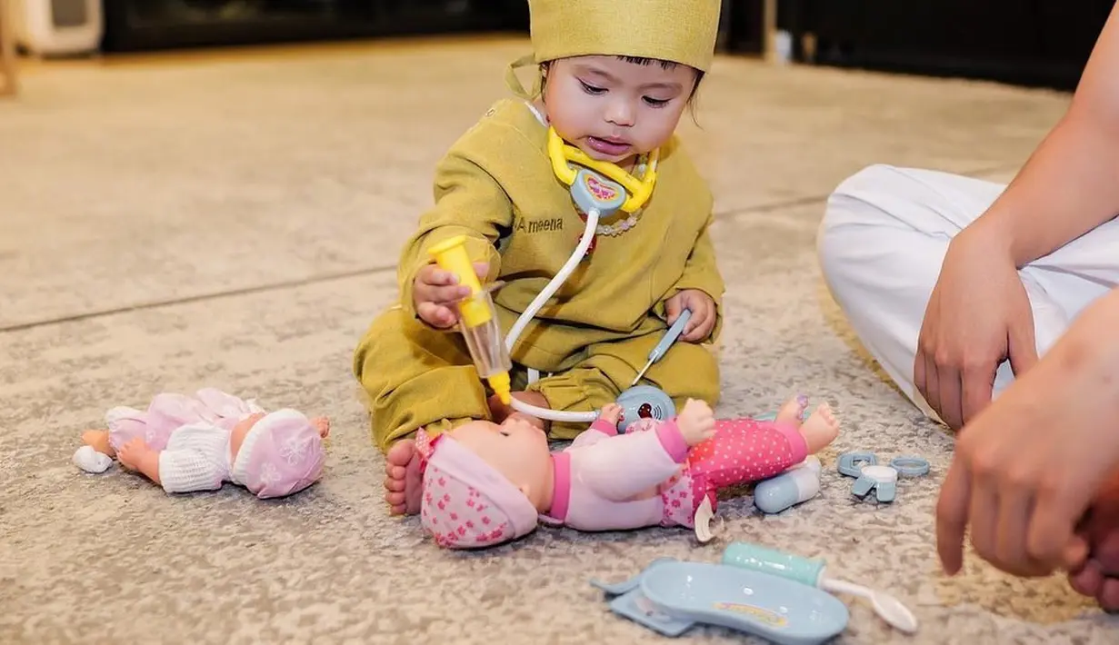 Potret berikut tidak kalah menggemaskan banyak netizen. Tampak, baby Ameena dandan ala dokter, ia memeriksa boneka mainannya.  [Instagram/ameenaatta]