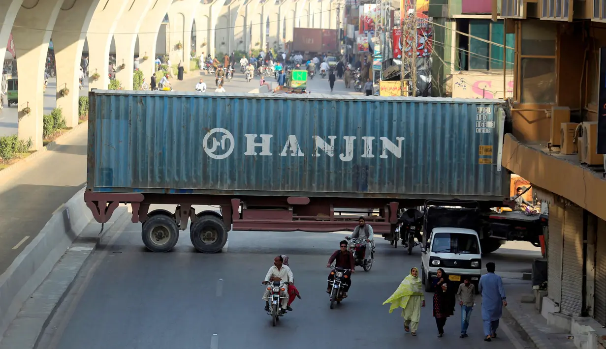 Sejumlah pengendara motor melewati kolong sebuah truk kontainer di Rawalpindi, Pakistan (28/10). Kejadian ini akibat sejumlah truk kontainer memblokir jalan raya selama demo yang digelar Awami Muslim League (AML). (Reuters/Faisal Mahmood)